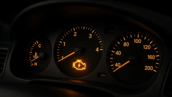 Foto panel instrumen mobil dengan lampu check engine berwarna oranye menyala di antara speedometer dan takometer