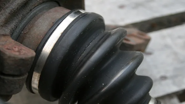 Foto mekanik menyorot senter ke karet boot CV joint yang sobek dan berlumur gemuk di roda depan hatchback merah