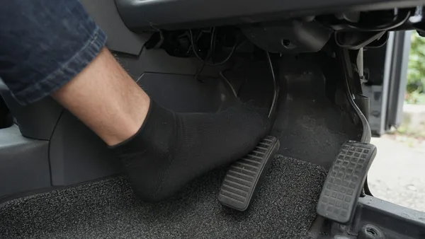 Foto kaki pengemudi menginjak pedal kopling di ruang kaki mobil kompak
